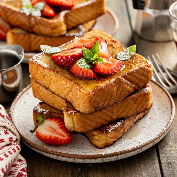 Stack of golden French toast topped with fresh strawberries, powdered sugar, and mint at Steve's Place.