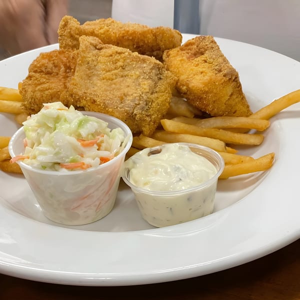 Steve's Place fried fish and chips with coleslaw and tartar sauce on a white plate.