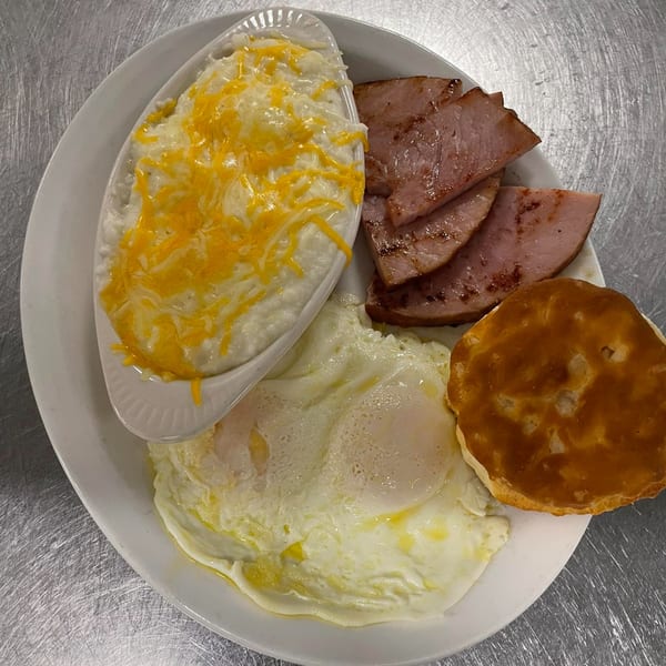 A breakfast plate with cheesy grits, grilled ham, fried eggs, and a biscuit from Steve's Place.