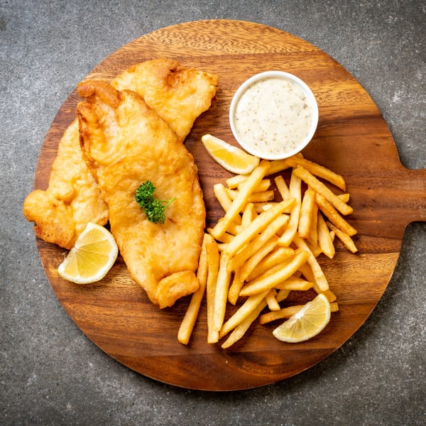Golden-brown fish and chips with tartar sauce, lemon wedges, and parsley on a wooden board.