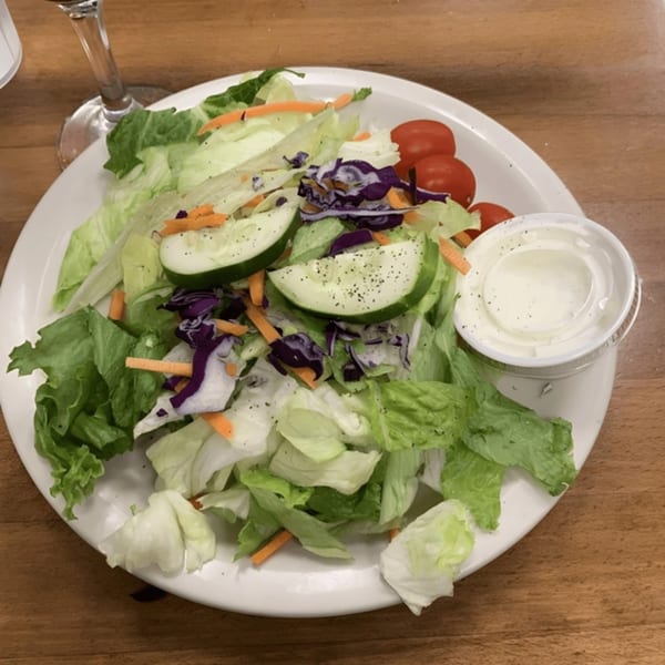 A fresh side salad with lettuce, cucumbers, carrots, red cabbage, tomatoes, and ranch dressing.